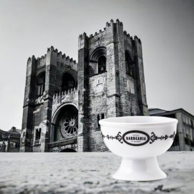 Taça branca em cerâmica decorada com texto e motivos florais em fundo de edifício histórico cinzento.
