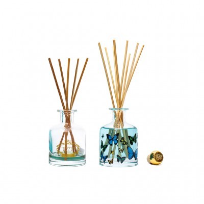 Difusores de varetas em frascos de vidro, um com líquido amarelo e outro decorado com borboletas, tampa dourada ao lado.
