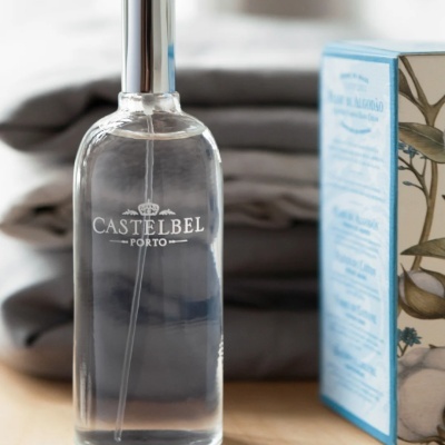 Frasco transparente de líquido e caixa azul decorada com tecidos cinzentos ao fundo.