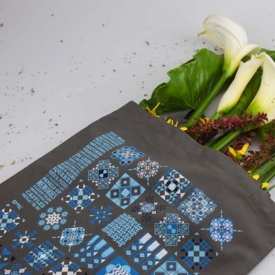 Saco cinza com padrão geométrico azul contendo flores brancas e verdes.