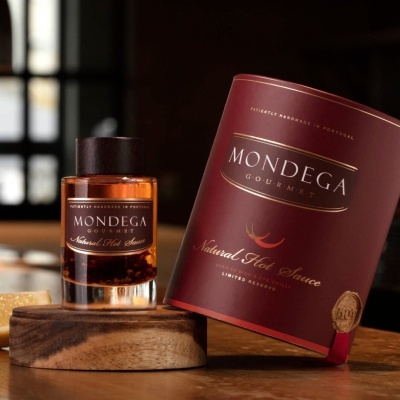 Frasco de molho picante e embalagem bordô MONDEGA Gourmet sobre base de madeira