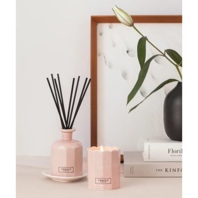 Vela e difusor de varetas rosa claro com etiquetas Portus Cale e vaso preto com flor branca