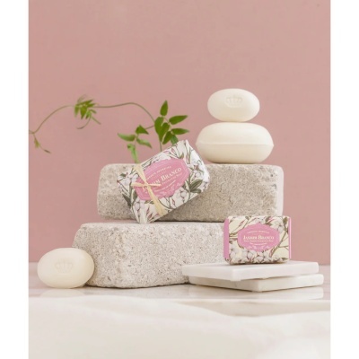 Sabonetes aromáticos Jasmine Branco e sabonetes brancos sobre pedra e base branca com fundo rosa e ramo verde.