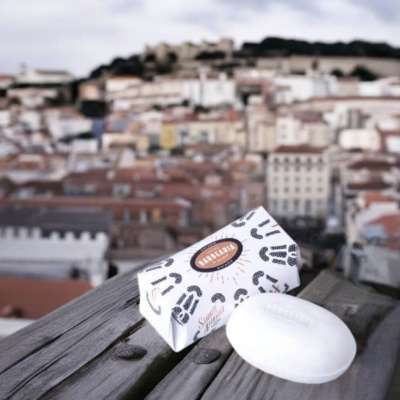 Sabonete branco oval e embalagem com padrão de bigodes sobre madeira, cidade desfocada ao fundo