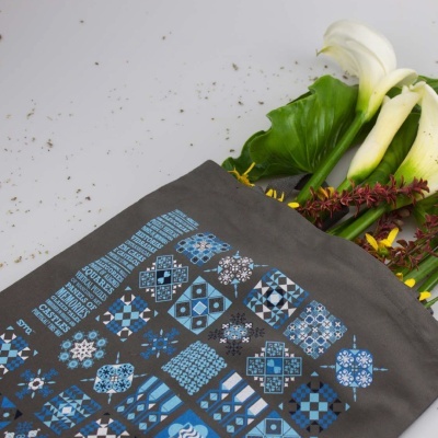 Saco de tecido cinzento com padrões azuis e brancos contendo flores e folhas verdes
