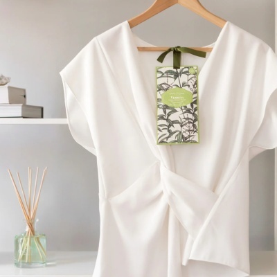 Blusa branca com detalhe franzido num cabide de madeira e etiqueta de folhas verdes