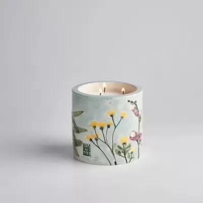 Vela decorativa em cerâmica com padrão floral e duas chamas acesas