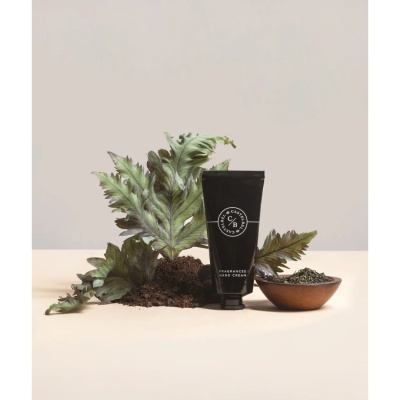 Tubo preto de creme para mãos com folhas verdes, terra e tigela de madeira com folhas secas.
