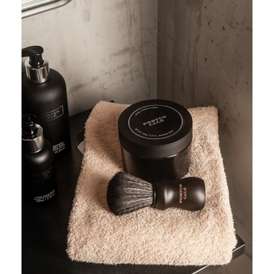 Produtos de barbear preto em toalha bege sobre balcão escuro