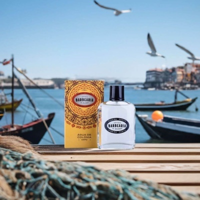Frasco e caixa de água de colónia Antiga Barbearia de Bairro em ambiente marítimo com barcos e gaivotas.
