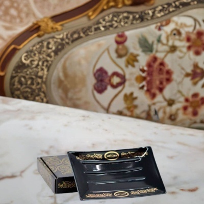 Cinzeiro cerâmico preto com decoração dourada e caixa sobre mesa de mármore