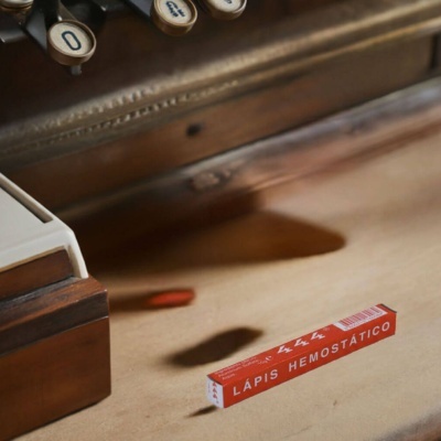 Caixa de lápis hemostático vermelha sobre superfície clara próxima a máquina de escrever antiga