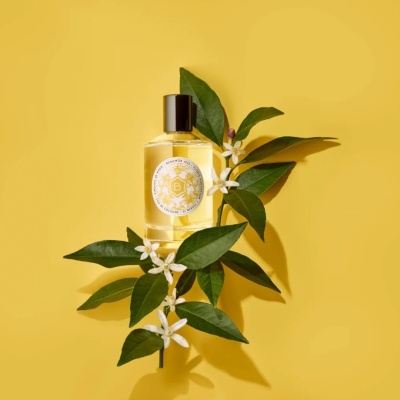 Frasco de perfume com flores e folhas verdes num fundo amarelo
