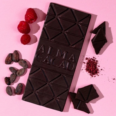 Barra de chocolate preto com framboesas e grãos de cacau sobre fundo rosa