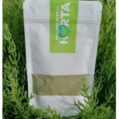 Embalagem branca resselável com pó verde e etiqueta SALICÓRNIA EM PÓ DA HORTA rodeada de plantas verdes