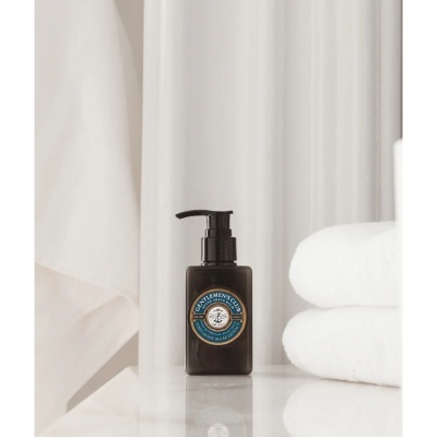Frasco de after shave balm preto com rótulo azul e dourado e duas toalhas brancas dobradas