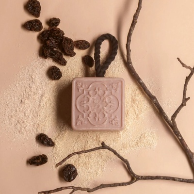 Sabonete quadrado cor de rosa com cordão preto e relevo ornamental em fundo bege