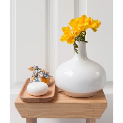 Vaso cerâmico branco com flores amarelas, sabonete branco e objeto embrulhado em tecido sobre mesa de madeira