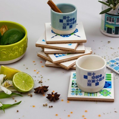 Dois copos pequenos com padrões azuis sobre bases decoradas com motivos geométricos e florais, com limão e especiarias à volta