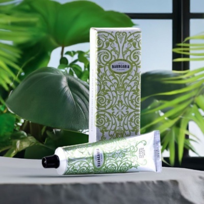 Produto cosmético BARBEARIA em tubo e embalagem branca com padrões verdes, com plantas ao fundo