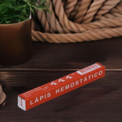 Lápis hemostático em caixa vermelha sobre mesa de madeira com planta e corda ao fundo