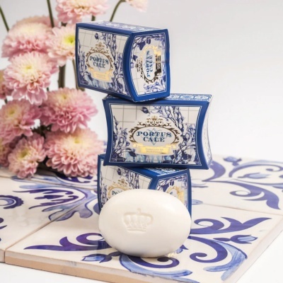 Sabonetes Portus Cale em caixas decorativas sobre azulejos com flores cor-de-rosa ao fundo.