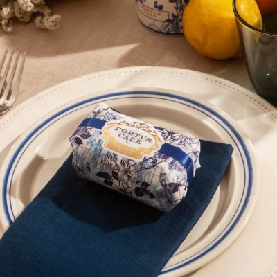 Sabonete embalado com padrão floral azul e branco sobre guardanapo azul em prato branco com borda azul