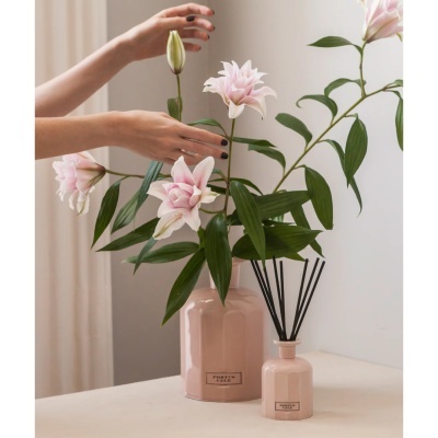 Vaso cerâmico rosa com flores artificiais e difusor de aromas rosa com varetas negras numa mesa clara