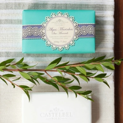 Sabonete aromático Castelbel em embalagem turquesa com etiqueta decorada e ramo verde sobre tecido riscado