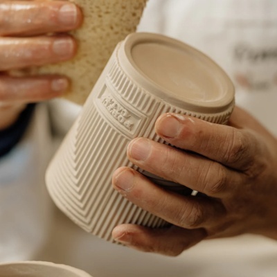 Caneca de cerâmica bege texturizada com relevo HANDMADE segurada por mãos
