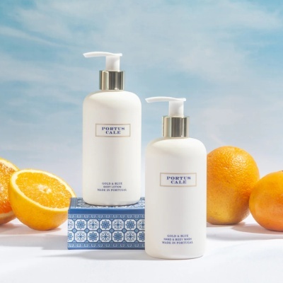Frascos de loção corporal e gel de mãos PORTUS CALE com laranjas e céu azul ao fundo.