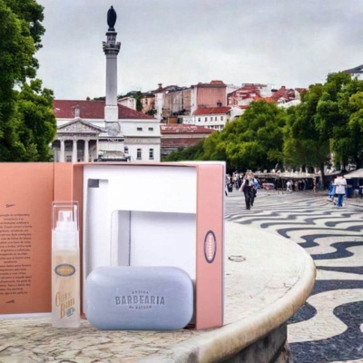 Produtos de barbear Antiga Barbearia de Bairro em caixa cor-de-rosa sobre calçada portuguesa com padrão preto e branco em ondas.