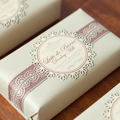 Sabonete embalado em papel branco com faixa rendada cor de vinho e etiqueta redonda decorativa