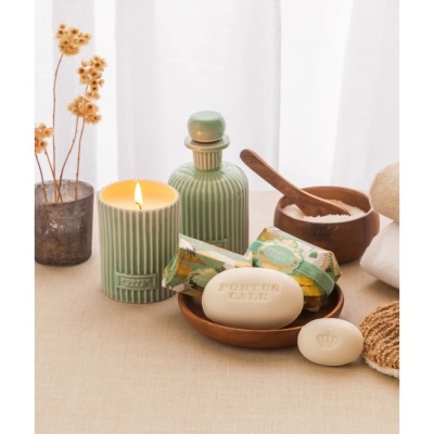 Conjunto de produtos de banho e aromaterapia com vela verde riscada com texto PORTUS CALE e sabonetes em contexto relaxante