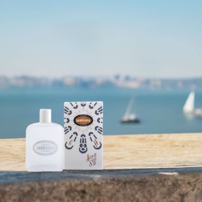 Frasco branco fosco e embalagem de after shave ANTIGA BARBEARIA DE BAIXO CHIADO em fundo exterior com mar e veleiros