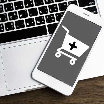 Smartphone branco com ícone de carrinho de compras no ecrã, sobre teclado de portátil prateado