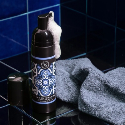 Frasco de sabonete espumante com etiqueta azul e toalha cinza sobre azulejos azuis