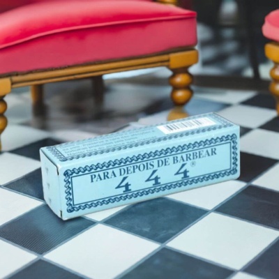 Embalagem azul clara para depois de barbear no chão de azulejos preto e branco com cadeiras vermelhas