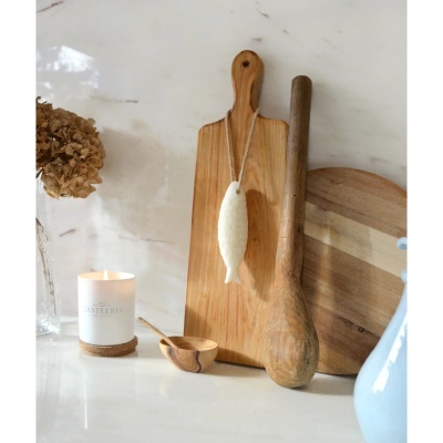 Utensílios de cozinha em madeira, vela branca CASTELBEL PORTO, esponja em forma de peixe pendurada, flor seca em vaso de vidro sobre bancada de mármore