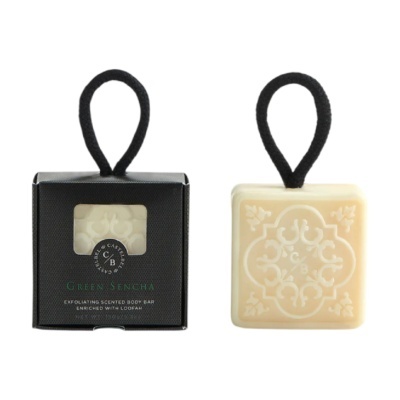 Sabão esfoliante para corpo com padrão decorativo, cordão preto e embalagem preta com texto.