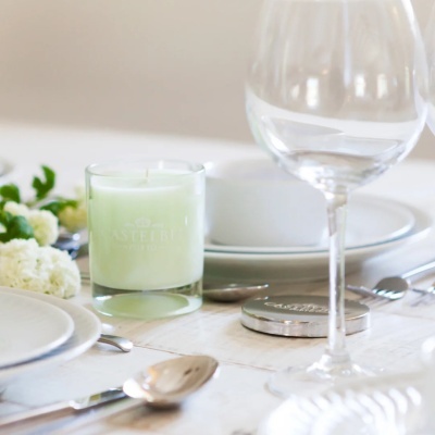 Vela verde clara numa mesa posta com pratos, talheres, flores e copo de vinho