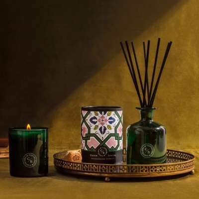 Conjunto com vela verde, difusor e embalagem colorida sobre tabuleiro metálico dourado