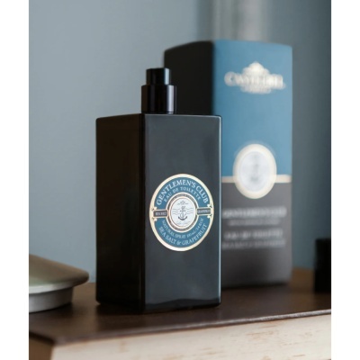 Frasco de eau de toilette preto com etiqueta azul em superfície de madeira com caixa ao fundo