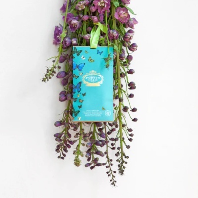 Pacote azul com estampas de borboletas pendurado sobre flores roxas