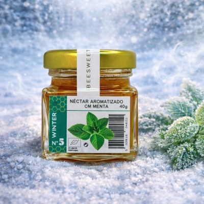 Frasco pequeno de néctar aromatizado com menta com tampa dourada sobre superfície branca e neve artificial.