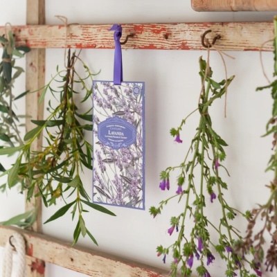Saqueta perfumada de lavanda pendurada entre ramos verdes e flores secas num suporte de madeira envelhecida