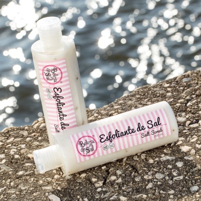 Frascos de esfoliante de sal com rótulos rosa e branco sobre rochas perto da água