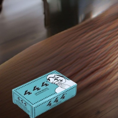 Caixa azul clara de after shave com ilustração de homem e texto 444 sobre mesa de madeira