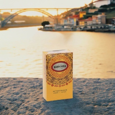 Embalagem amarela de after shave Antiga Barbearia de Bairro com padrões vermelhos e pretos junto a rio e ponte ao pôr do sol.