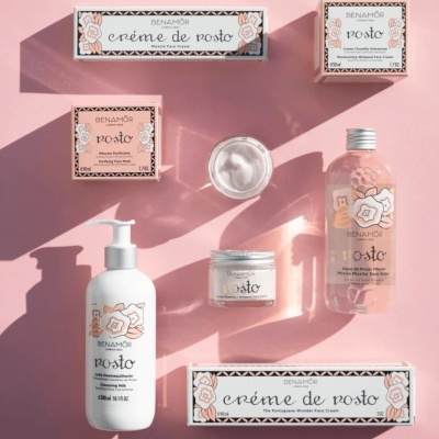 Produtos de cuidados faciais BENAMÔR embalados em cores rosa e branco com decoração floral sobre fundo rosa.
